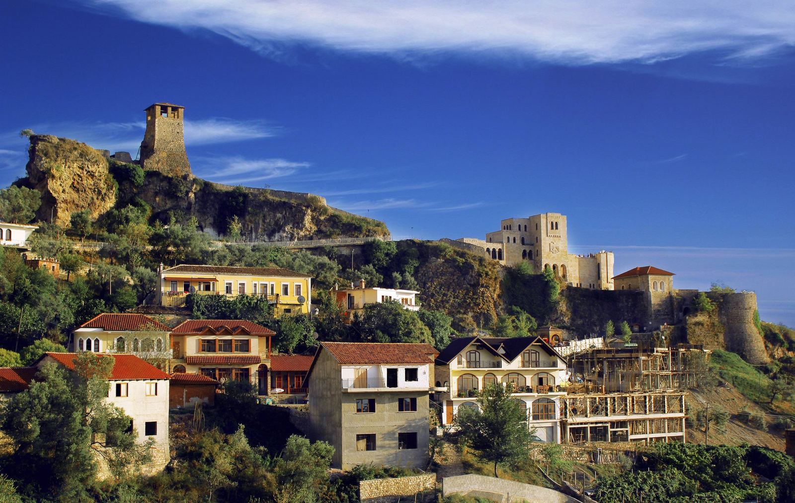 Stone houses below the castle walls and clock tower of Krujë under a blue sky