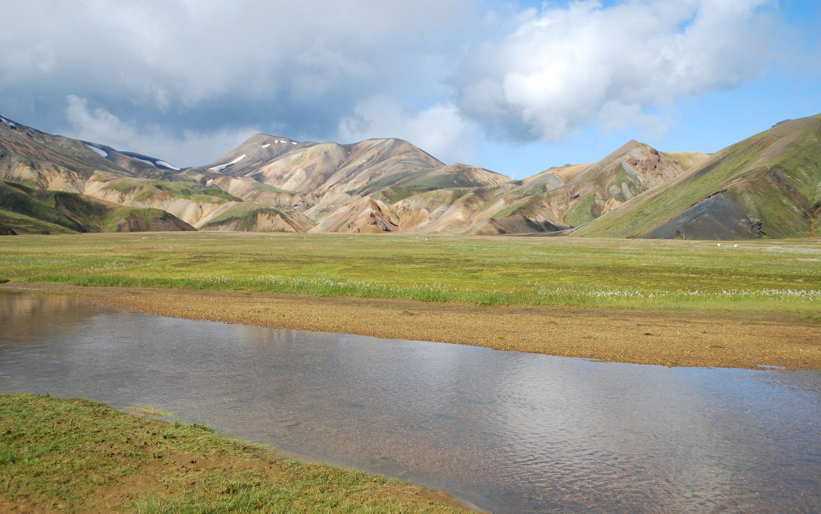 Striped rhyolite mountains in yellow, pink and green behind a wet plain at Landmannalaugar