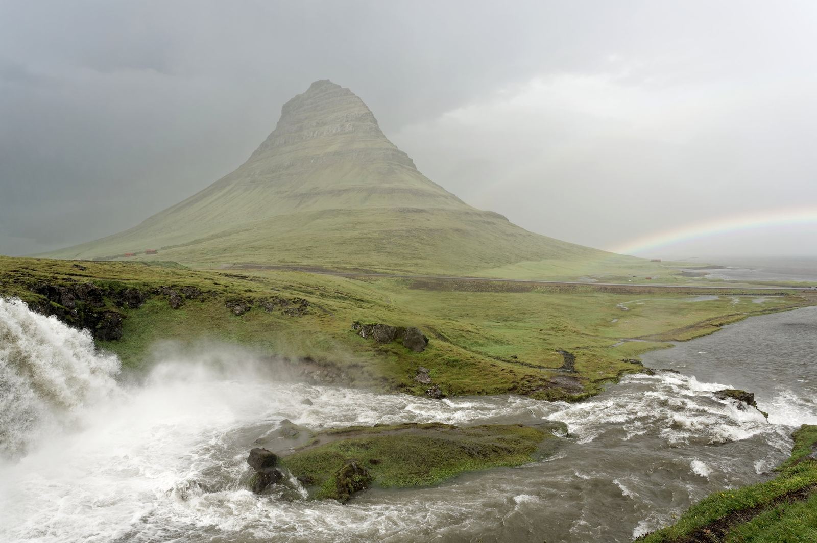 De puntige berg Kirkjufell boven groene weiden met de waterval Kirkjufellsfoss op de voorgrond