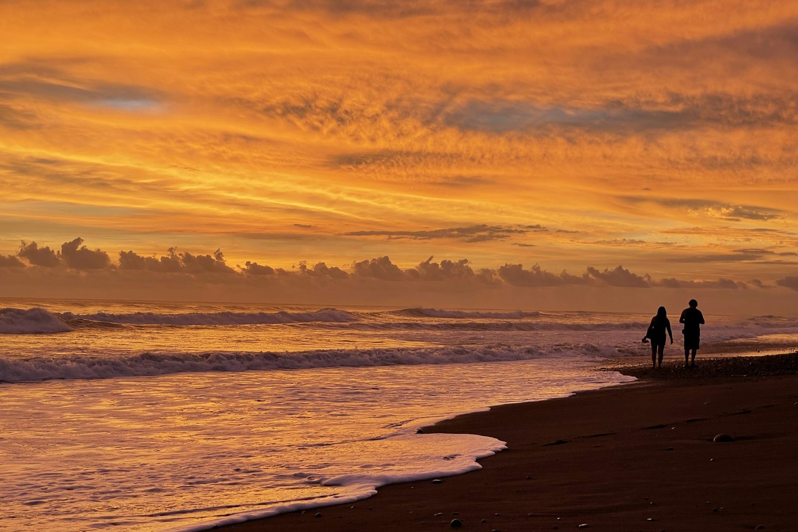 A couple walking along the surf of Playa Dominical at sunset, Costa Rica