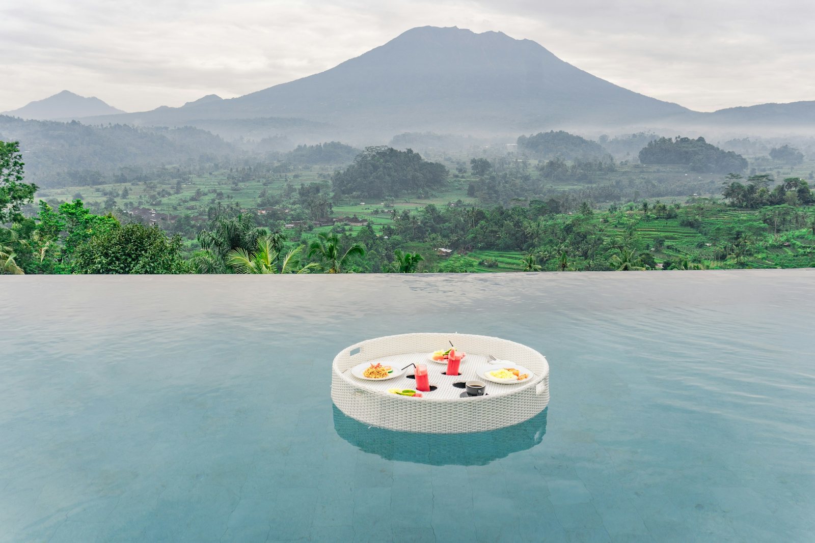 A floating breakfast in an infinity pool with rice fields and a volcano behind, Bali