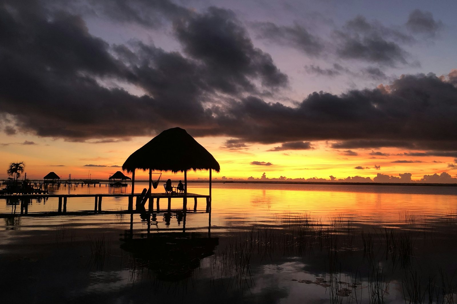 A thatched pavilion on a jetty in the Bacalar lagoon at sunset