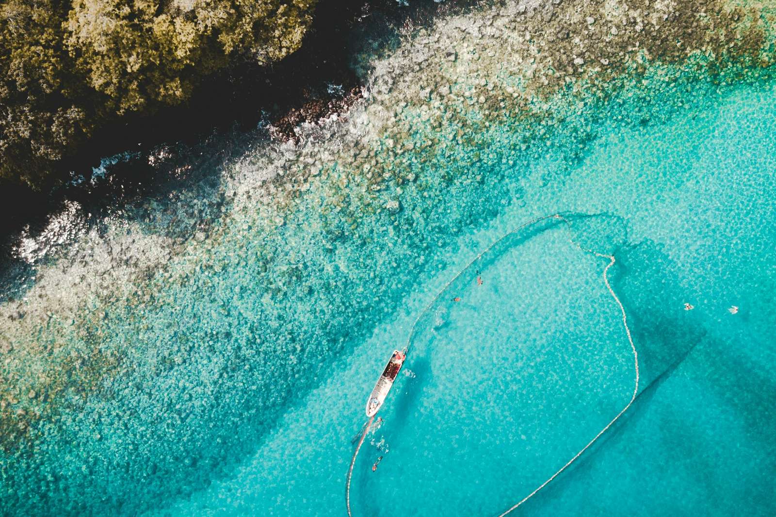 Aerial view of a fishing boat in turquoise water along the forested coast of São Tomé