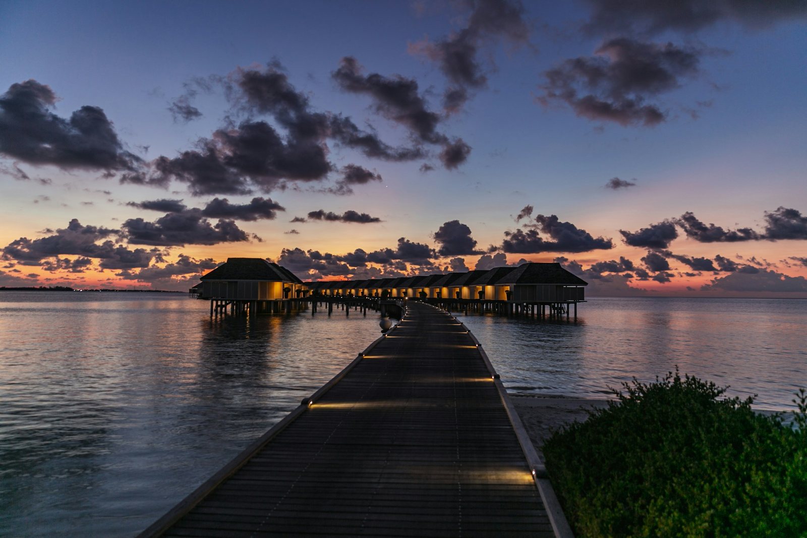 A wooden jetty leading to overwater villas above the lagoon at sunset, Maldives